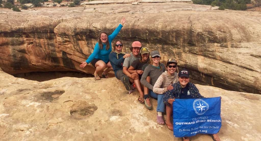 A group of people sit in a row near the edge of a canyon and smile for the photo. 